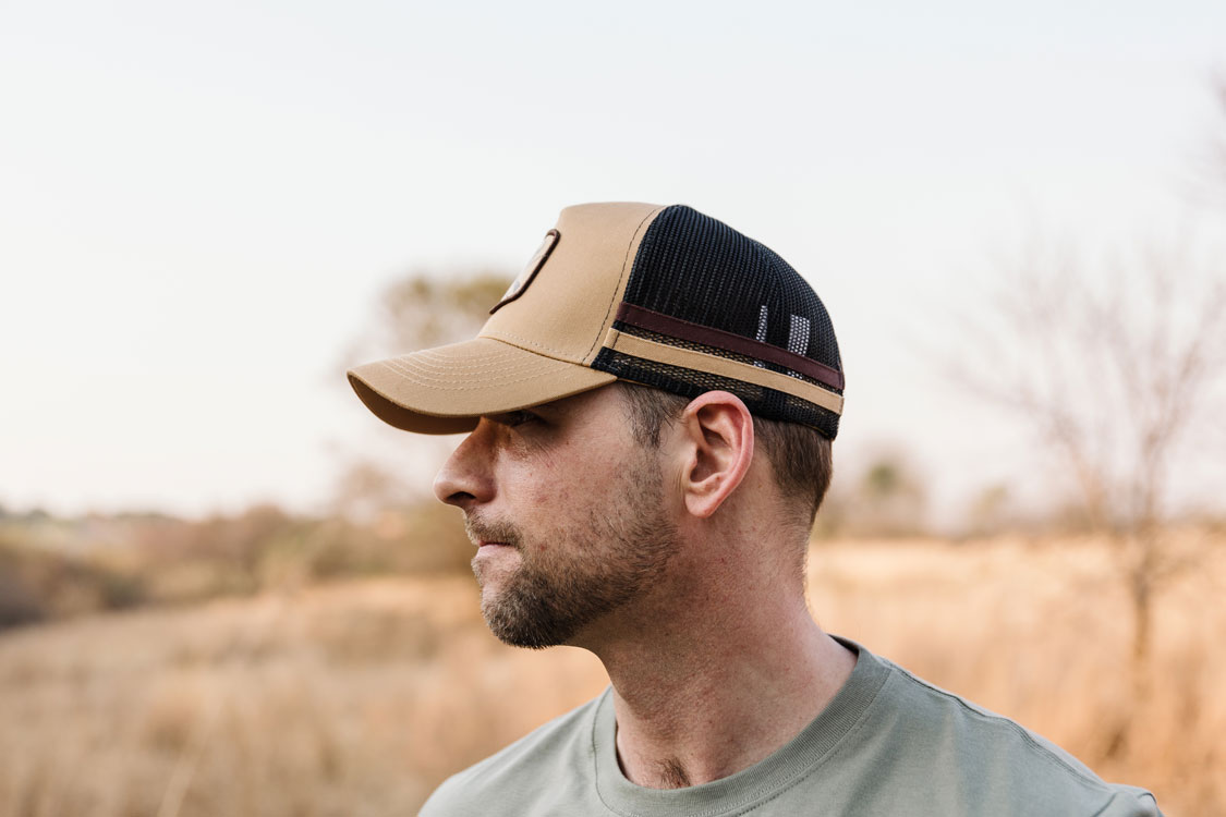 Man wearing a tan REPUBLK trucker cap in the veld
