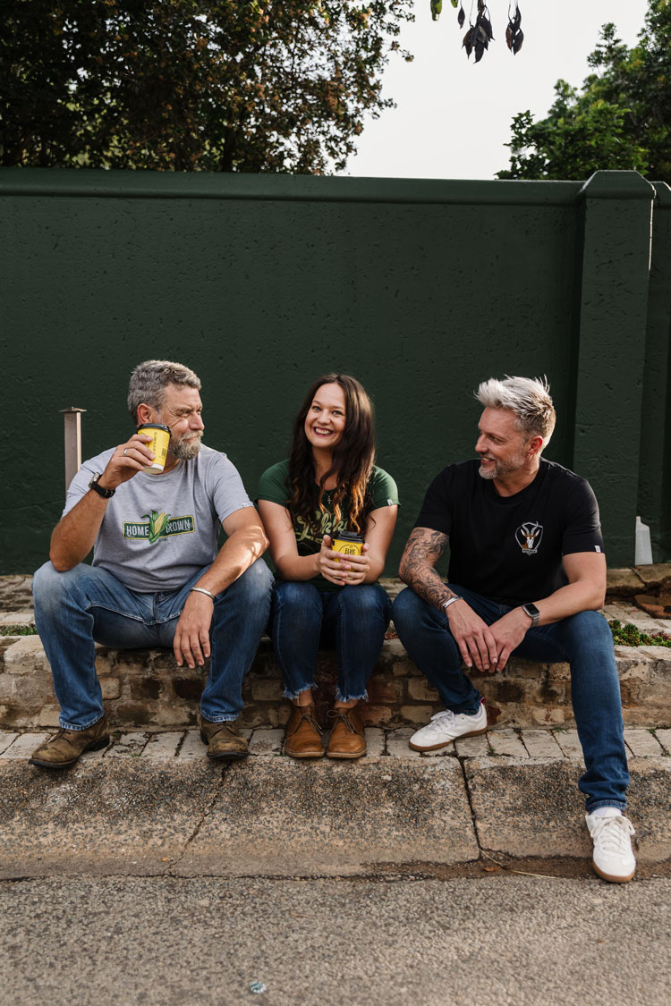 Three friends in REPUBLK tees sharing coffee against a deep green wall