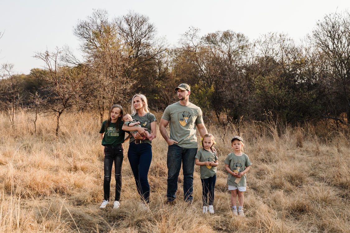 Family in matching olive REPUBLK tees standing in golden bushveld grass